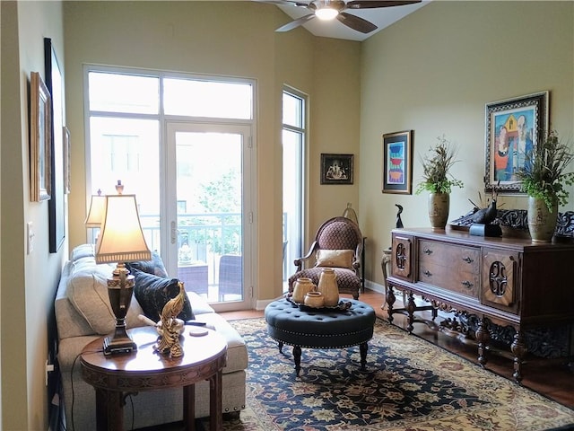 sitting room featuring baseboards, wood finished floors, ceiling fan, and a towering ceiling