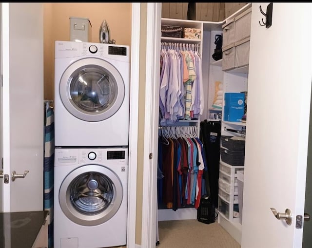 clothes washing area featuring stacked washer and clothes dryer, laundry area, and carpet
