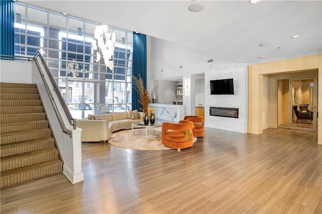 living room with stairs, a large fireplace, a wall of windows, and wood finished floors