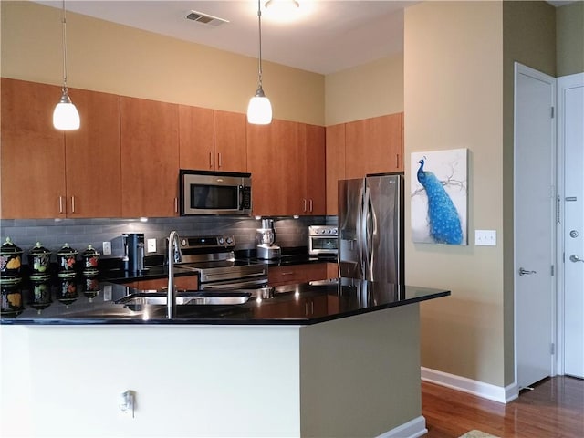 kitchen with appliances with stainless steel finishes, dark countertops, a sink, visible vents, and a peninsula