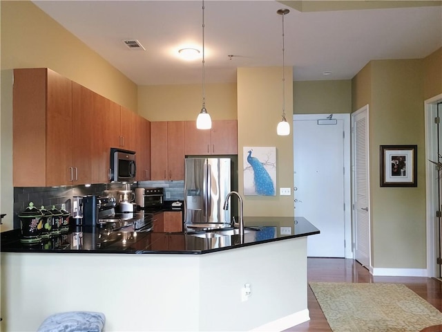 kitchen featuring a sink, dark countertops, stainless steel appliances, dark wood-type flooring, and a peninsula