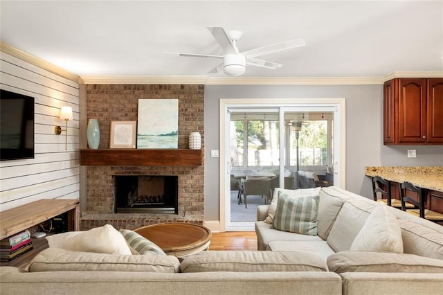 living room featuring crown molding, ceiling fan, wood walls, and a brick fireplace