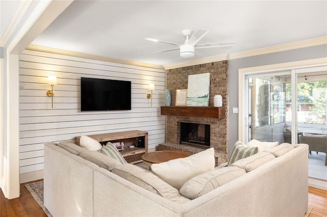 living room with hardwood / wood-style floors, wood walls, ceiling fan, ornamental molding, and a fireplace