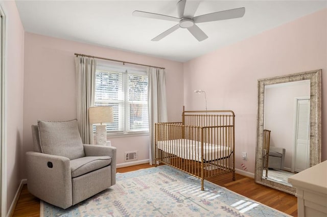 bedroom with hardwood / wood-style floors, ceiling fan, and a crib