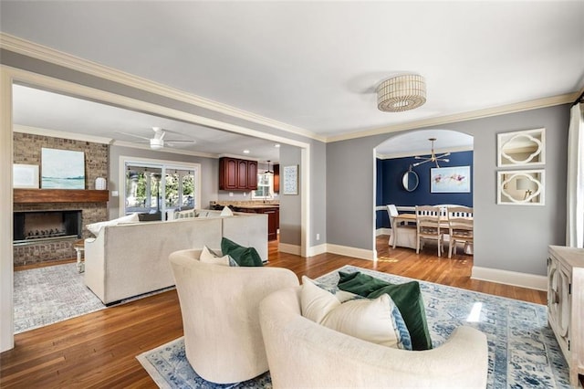 living room featuring ceiling fan, a fireplace, wood-type flooring, and ornamental molding