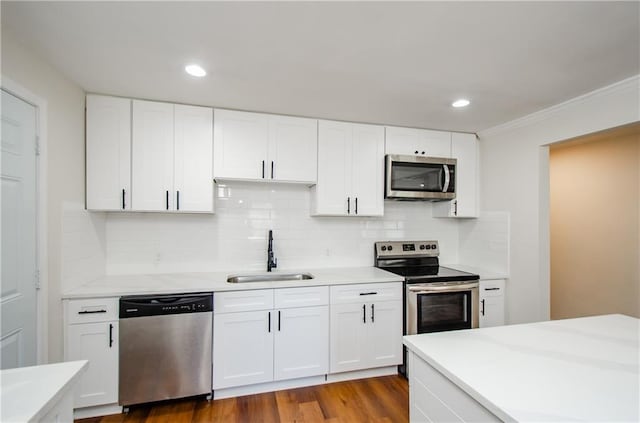 kitchen with appliances with stainless steel finishes, sink, white cabinets, hardwood / wood-style flooring, and decorative backsplash