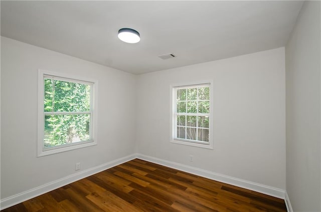 empty room featuring baseboards, dark wood finished floors, and visible vents