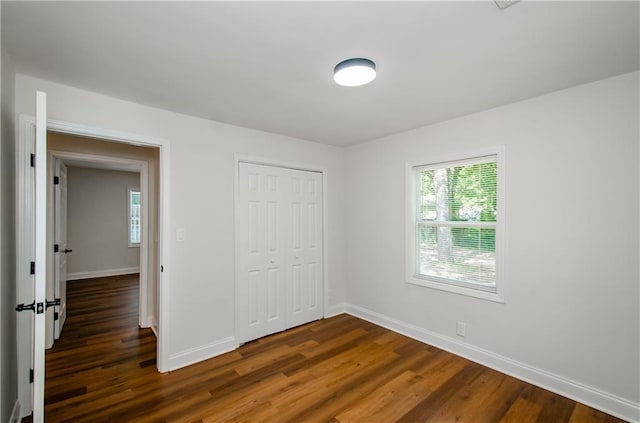 unfurnished bedroom with baseboards, a closet, dark wood-style floors, and multiple windows
