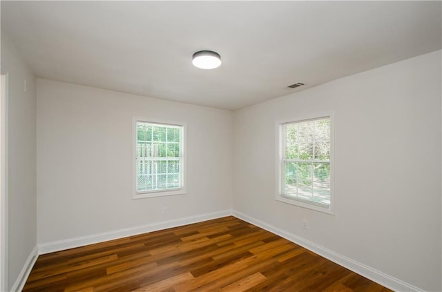 spare room featuring dark wood-style flooring, baseboards, visible vents, and plenty of natural light