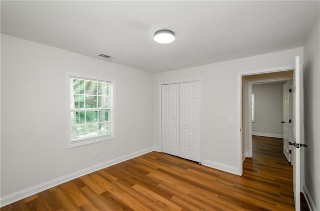 unfurnished bedroom featuring visible vents, baseboards, wood finished floors, and a closet