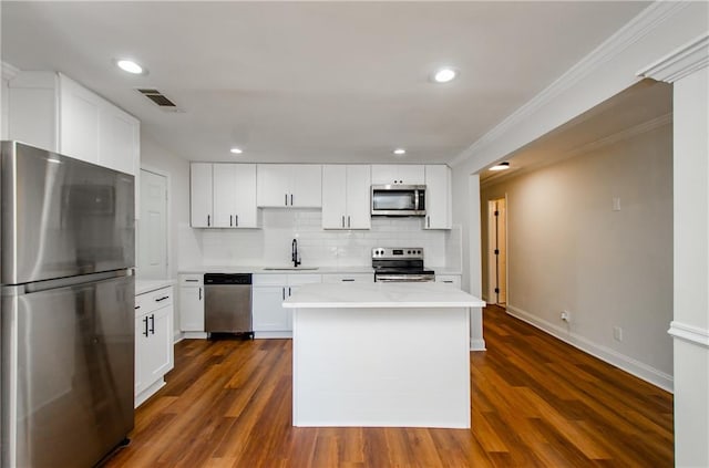 kitchen with white cabinets, appliances with stainless steel finishes, ornamental molding, dark wood-type flooring, and sink