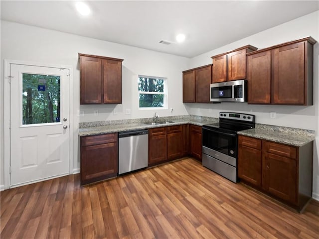 kitchen with wood-type flooring, light stone countertops, stainless steel appliances, and sink