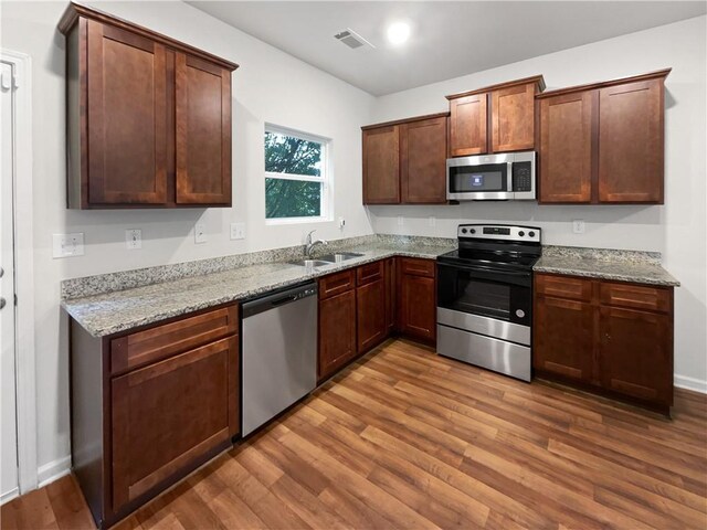 kitchen with light hardwood / wood-style flooring, stainless steel appliances, light stone countertops, and sink