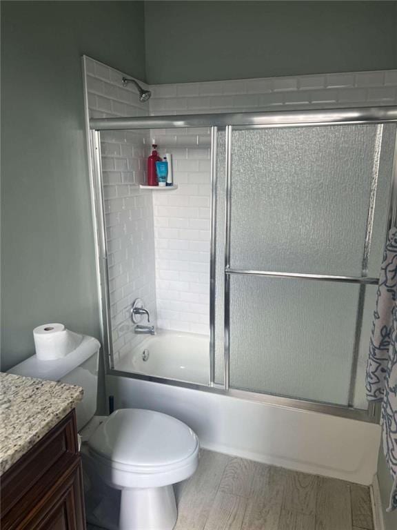 full bathroom featuring wood-type flooring, shower / bath combination with glass door, vanity, and toilet