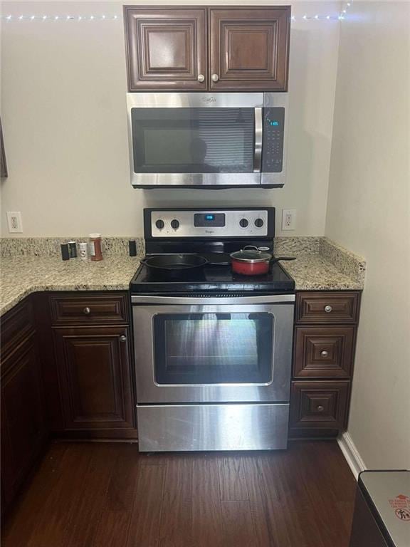 kitchen with dark brown cabinetry, dark hardwood / wood-style flooring, stainless steel appliances, and light stone counters