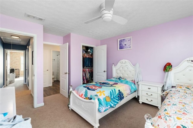 carpeted bedroom featuring a walk in closet, a textured ceiling, ceiling fan, and a closet