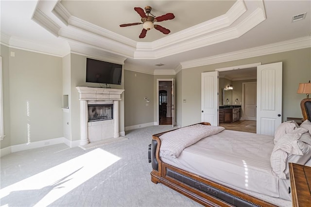 carpeted bedroom featuring crown molding, a tray ceiling, a fireplace with flush hearth, baseboards, and ensuite bathroom