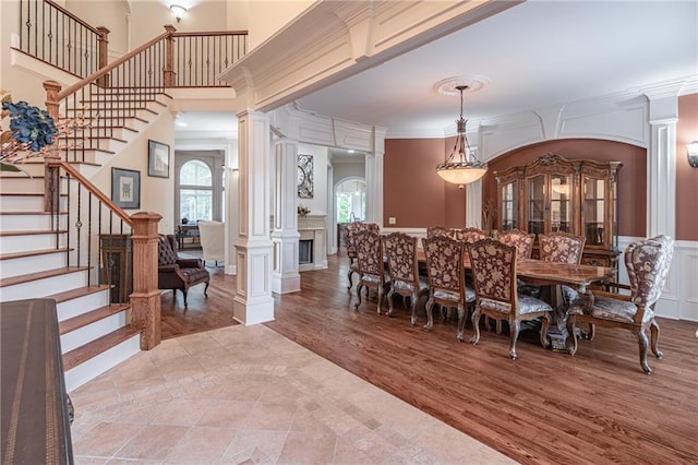 dining area featuring plenty of natural light, a decorative wall, ornate columns, stairway, and crown molding