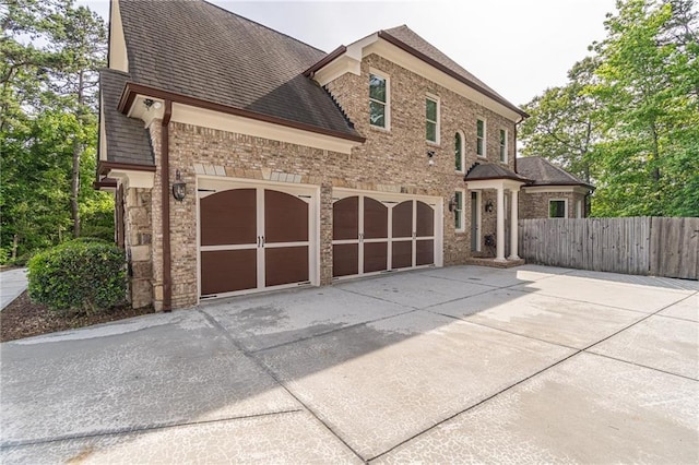 view of front of house with concrete driveway, fence, roof with shingles, and brick siding