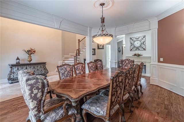 dining space featuring decorative columns, stairs, wood finished floors, and ornamental molding