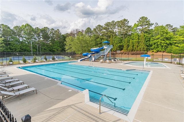 community pool featuring a water slide, fence, and view of scattered trees