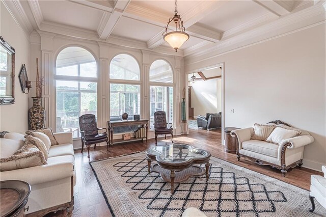 living area with coffered ceiling, beam ceiling, wood finished floors, crown molding, and a ceiling fan