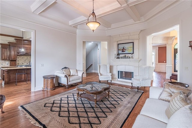 living area with coffered ceiling, beamed ceiling, ornamental molding, wood finished floors, and a large fireplace