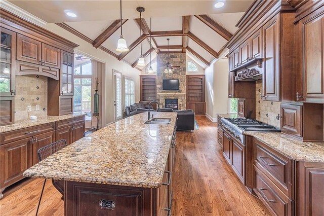 kitchen with a sink, open floor plan, a stone fireplace, an island with sink, and stainless steel gas cooktop