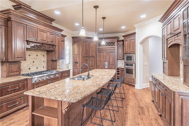 kitchen featuring a sink, stainless steel appliances, arched walkways, a kitchen bar, and light stone counters