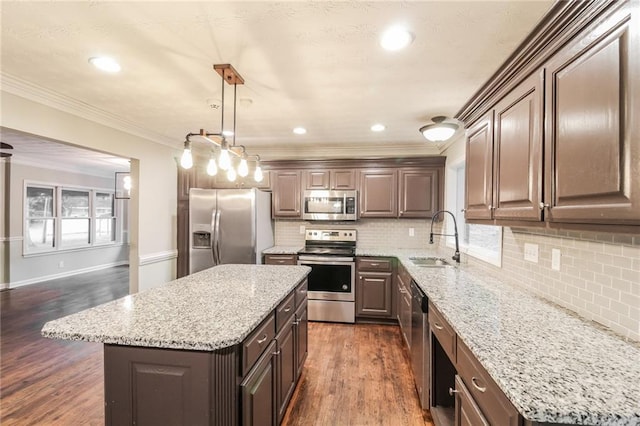 kitchen with appliances with stainless steel finishes, dark wood-type flooring, ornamental molding, and a center island