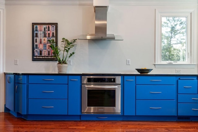 kitchen with dark wood-style flooring, stainless steel oven, modern cabinets, blue cabinets, and wall chimney exhaust hood