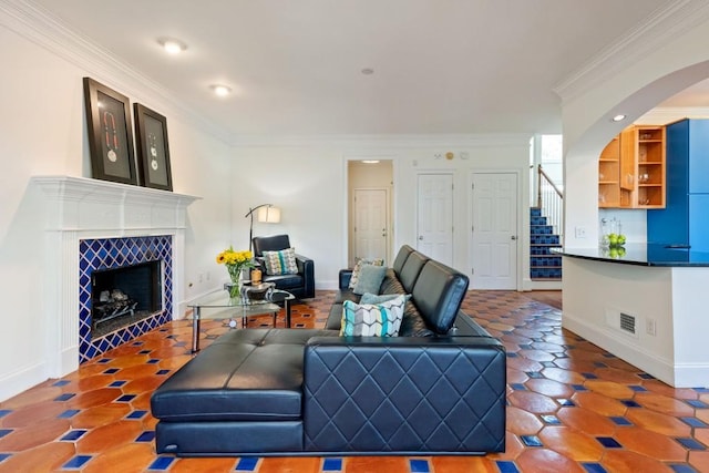 living area featuring a tile fireplace, visible vents, baseboards, stairs, and ornamental molding