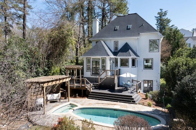 rear view of house featuring a shingled roof, a chimney, a deck, a pool with connected hot tub, and stucco siding