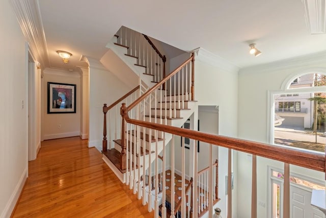 hall featuring ornamental molding, light wood-style floors, baseboards, and stairs