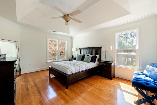 bedroom with ornamental molding, a tray ceiling, light wood-style flooring, and baseboards