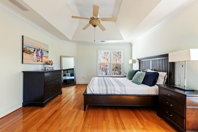 bedroom with baseboards, ornamental molding, a raised ceiling, and light wood-style floors