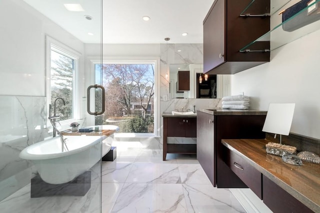 full bath with marble finish floor, tile walls, recessed lighting, vanity, and a freestanding tub