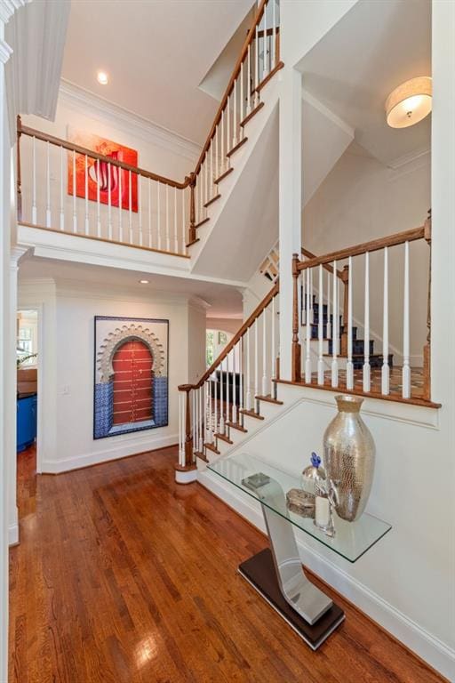 stairway with wood finished floors, a towering ceiling, baseboards, ornamental molding, and a wealth of natural light