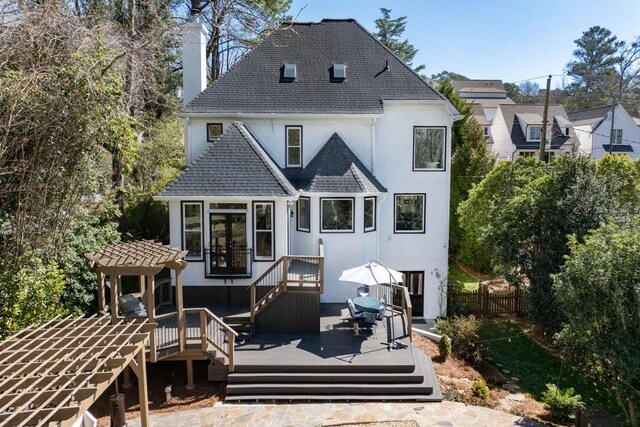 rear view of property featuring a chimney, fence, a deck, and stucco siding