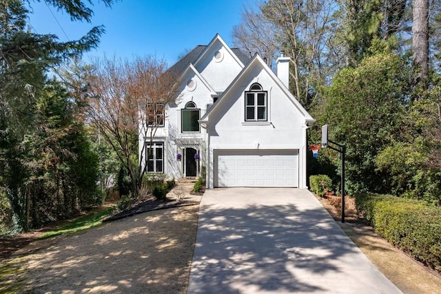 view of front of home featuring driveway, an attached garage, a chimney, and stucco siding