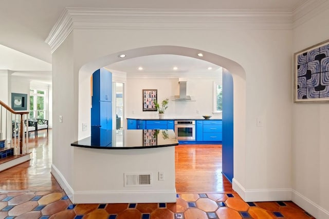 interior space featuring arched walkways, blue cabinetry, visible vents, oven, and wall chimney exhaust hood