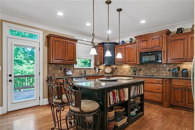 kitchen featuring decorative light fixtures, a wealth of natural light, hardwood / wood-style floors, dark stone countertops, and a kitchen island