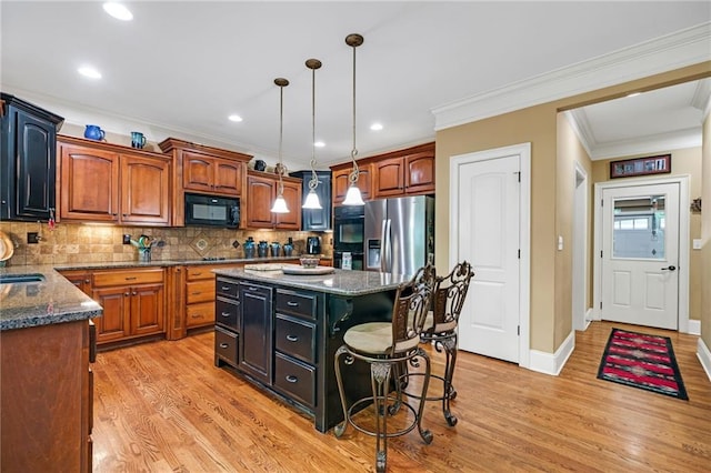 kitchen featuring light hardwood / wood-style flooring, decorative light fixtures, a center island, dark stone countertops, and black appliances