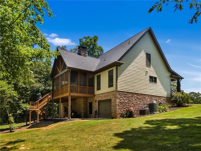 rear view of house with a garage, a sunroom, a lawn, and central AC