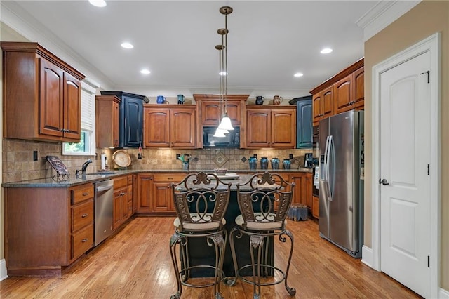 kitchen with crown molding, pendant lighting, appliances with stainless steel finishes, a kitchen island, and light hardwood / wood-style floors