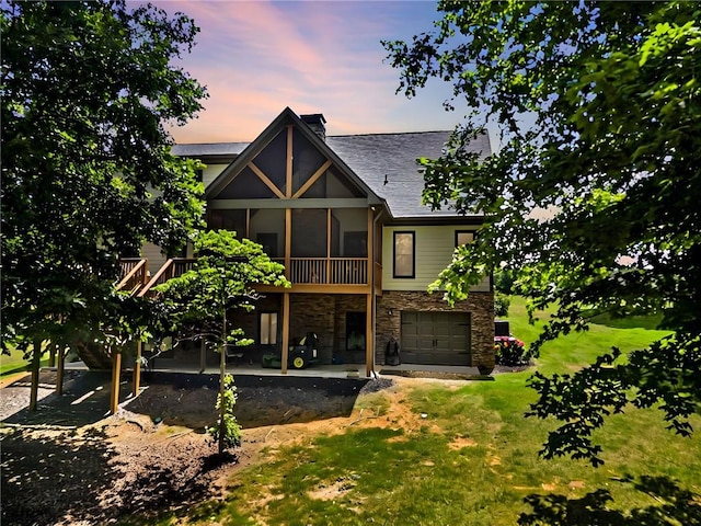 back house at dusk featuring a sunroom, a patio area, a garage, a wooden deck, and a lawn