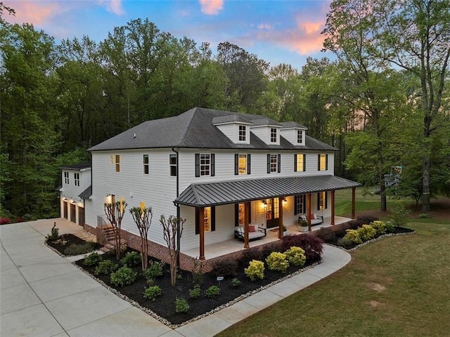 back house at dusk featuring a porch, a garage, and a yard