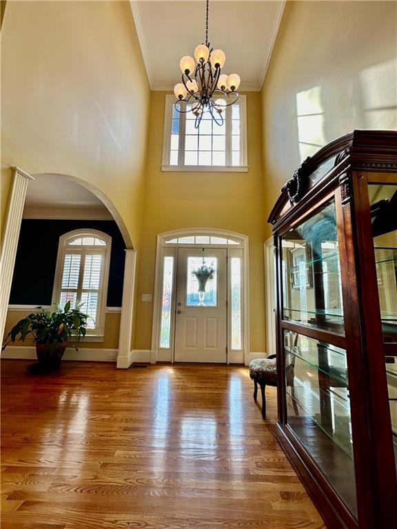 entrance foyer with baseboards, ornamental molding, arched walkways, and wood finished floors