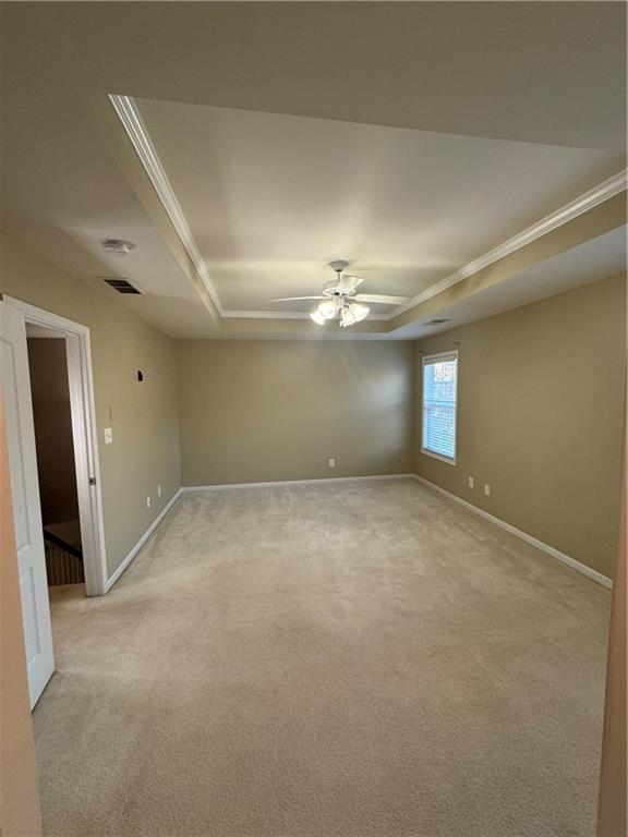 carpeted spare room featuring a tray ceiling and ceiling fan