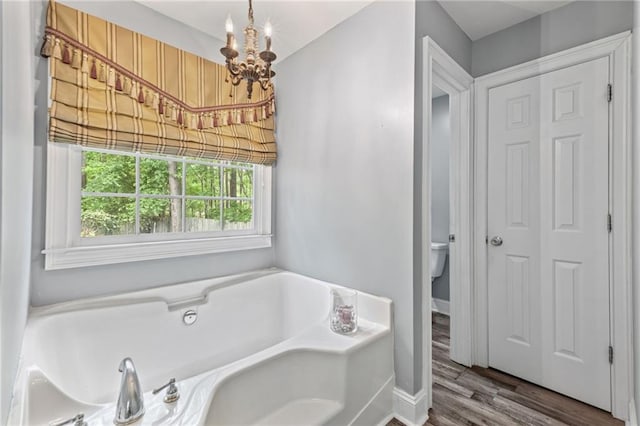 bathroom featuring an inviting chandelier, a garden tub, toilet, and wood finished floors